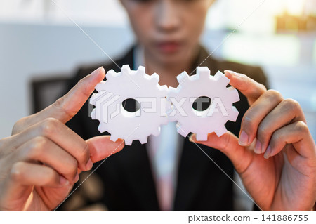 Business person holding two white gears together in front of face, teamwork, connection and planning 141886755