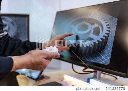 Engineer holding a gear and pointing at a 3d gear model on a monitor Engineer holding a gear and pointing at a 3d gear model on a monitor 141886770