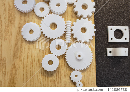 White plastic gears and small mechanical parts arranged on wood and black surface, engineering, assembly, and industrial design concept White plastic gears and small mechanical parts arranged on wood and black surface, engineering, assembly, and industrial design concept 141886788