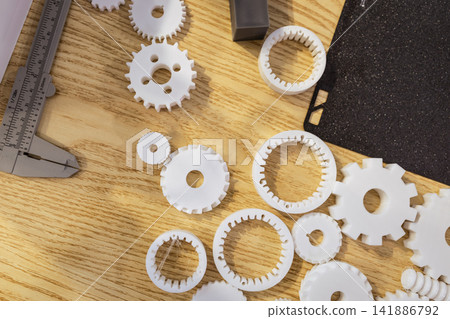 White plastic gear prototypes and measuring tools on a wooden workbench, seen from above White plastic gear prototypes and measuring tools on a wooden workbench, seen from above 141886792