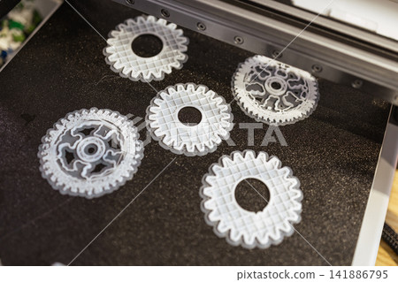 Several 3d printed gear parts arranged on a printer build plate during the making of plastic prototypes Several 3d printed gear parts arranged on a printer build plate during the making of plastic prototypes 141886795