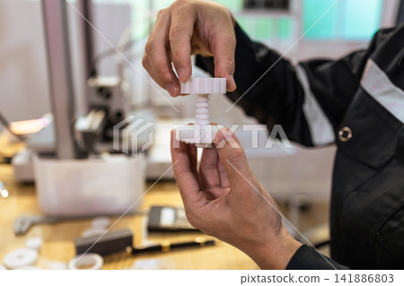 Hands holding a small white 3d printed gear part in a workshop Hands holding a small white 3d printed gear part in a workshop 141886803