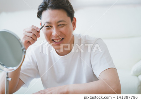 Men's makeup for middle-aged men: Drawing eyebrows with an eyebrow pencil while smiling. Men's makeup for middle-aged men: Drawing eyebrows with an eyebrow pencil while smiling. 141887786
