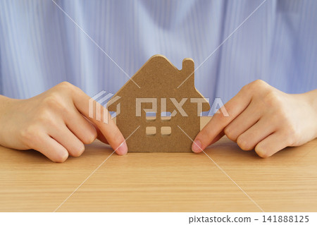 A young woman's hands touch a model of a house on a table. A young woman's hands touch a model of a house on a table. 141888125