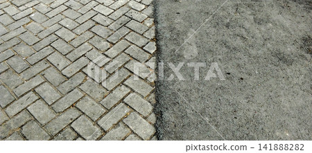 Herringbone-patterned paving blocks meeting a rough asphalt road surface. Herringbone-patterned paving blocks meeting a rough asphalt road surface. 141888282