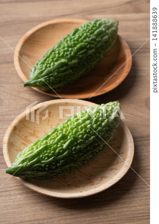 Fresh bitter gourd or bitter melon in a natural plate on a wooden background Fresh bitter gourd or bitter melon in a natural plate on a wooden background 141888639