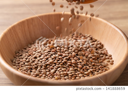 Raw green lentils pouring into a wooden bowl, high protein plant-based food and meat alternative Raw green lentils pouring into a wooden bowl, high protein plant-based food and meat alternative 141888659