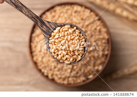 Close-up of whole wheat grain in a wooden spoon, Food ingredients, Top view Close-up of whole wheat grain in a wooden spoon, Food ingredients, Top view 141888674