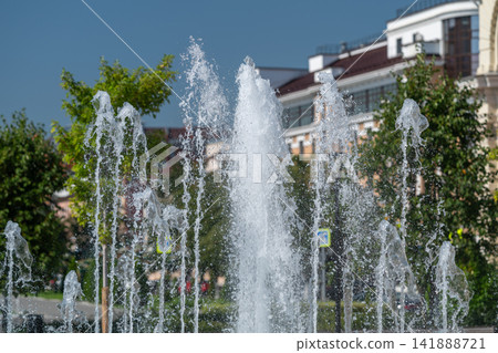 Dancing streams of water create a vibrant spectacle in the sunny park surrounded by lush greenery Dancing streams of water create a vibrant spectacle in the sunny park surrounded by lush greenery 141888721