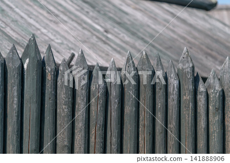 Old wooden fence with sharp tops standing tall against a clear blue sky in a quiet outdoors setting Old wooden fence with sharp tops standing tall against a clear blue sky in a quiet outdoors setting 141888906