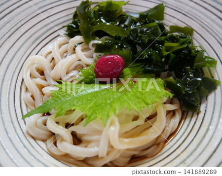 Cold udon noodles served on a glass plate with seaweed, pickled plums, and perilla leaves. Cold udon noodles served on a glass plate with seaweed, pickled plums, and perilla leaves. 141889289