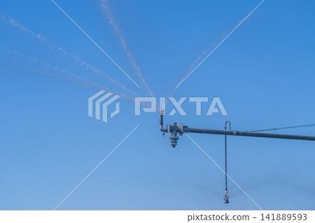 Water sprayers glistening under the bright blue sky during warm afternoon in a lush green field Water sprayers glistening under the bright blue sky during warm afternoon in a lush green field 141889593