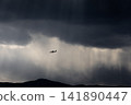 The silhouette of an airplane flying towards the light in a break in the stormy sky and clouds. 141890447