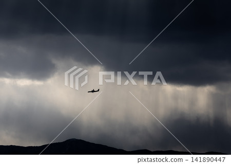 The silhouette of an airplane flying towards the light in a break in the stormy sky and clouds. The silhouette of an airplane flying towards the light in a break in the stormy sky and clouds. 141890447
