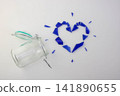 A small glass jar with a lid and a clasp lock fell next to a heart made of blue glass shards on a white background. The concept of love and separation. 141890655