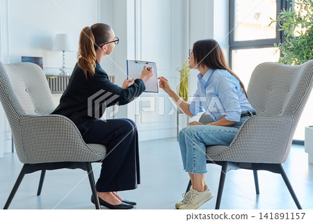 Female psychologist showing clipboard document to client during consultation Female psychologist showing clipboard document to client during consultation 141891157