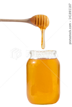 Liquid honey dripping from a wooden honey spoon into a glass jar filled with honey Liquid honey dripping from a wooden honey spoon into a glass jar filled with honey 141891187