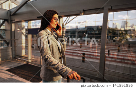 Busy Female Traveler Making Phone Call Outside Airport Terminal at Golden Hour Holding Luggage in Warm Cinematic Side Profile Shot Busy Female Traveler Making Phone Call Outside Airport Terminal at Golden Hour Holding Luggage in Warm Cinematic Side Profile Shot 141891856