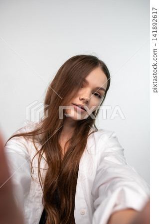 Young woman with natural long brown hair taking a selfie, looking at camera and embracing modern connection and authenticity Young woman with natural long brown hair taking a selfie, looking at camera and embracing modern connection and authenticity 141892617