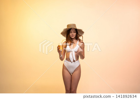 Young woman enjoying summer vacation, wearing white bikini and straw hat, holding refreshing cocktail drink Young woman enjoying summer vacation, wearing white bikini and straw hat, holding refreshing cocktail drink 141892634