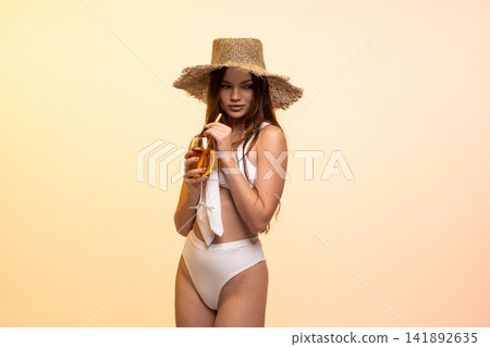 Young woman enjoying summer vacation, wearing a straw hat and white bikini, drinking a refreshing cocktail Young woman enjoying summer vacation, wearing a straw hat and white bikini, drinking a refreshing cocktail 141892635