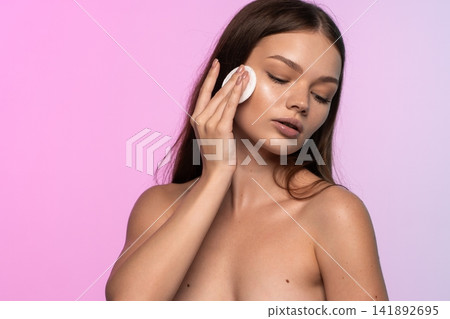 Woman cleansing bare skin with a cotton pad, caring for her face and achieving glowing, natural beauty 141892695