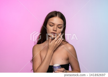 Woman applying cream to her face, eyes closed, maintaining beauty and healthy skincare routine Woman applying cream to her face, eyes closed, maintaining beauty and healthy skincare routine 141892697