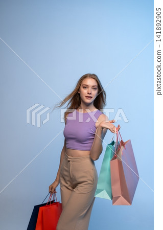 Young woman carrying colorful shopping bags on a light blue background, representing consumerism, fashion, and discount deals 141892905