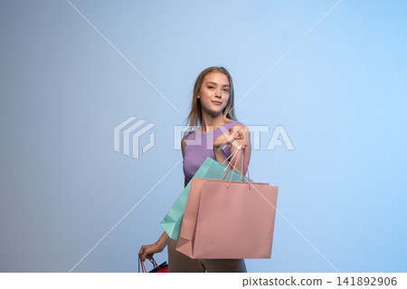 Young woman enjoying retail therapy, carrying colorful shopping bags after successful purchase on blue background Young woman enjoying retail therapy, carrying colorful shopping bags after successful purchase on blue background 141892906