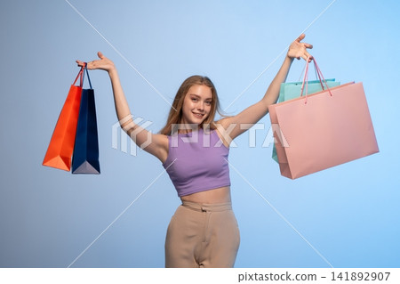 Young woman smiling, raising arms, holding various shopping bags, celebrating successful retail therapy and consumerism Young woman smiling, raising arms, holding various shopping bags, celebrating successful retail therapy and consumerism 141892907