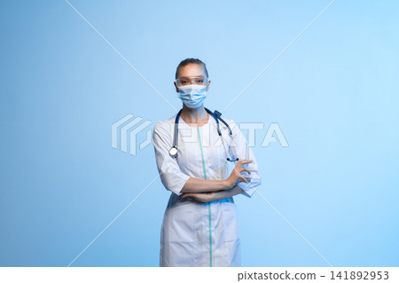 Healthcare professional standing with stethoscope, medical mask, safety glasses and syringe, ready for vaccination or injection Healthcare professional standing with stethoscope, medical mask, safety glasses and syringe, ready for vaccination or injection 141892953