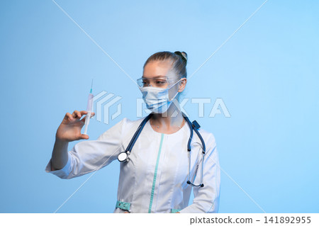 Medical professional holding a syringe wearing a mask and goggles, preparing vaccine or injection for healthcare treatment Medical professional holding a syringe wearing a mask and goggles, preparing vaccine or injection for healthcare treatment 141892955