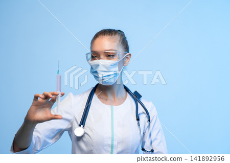 Healthcare worker in protective gear holding a syringe, preparing vaccine for injection or drug treatment Healthcare worker in protective gear holding a syringe, preparing vaccine for injection or drug treatment 141892956
