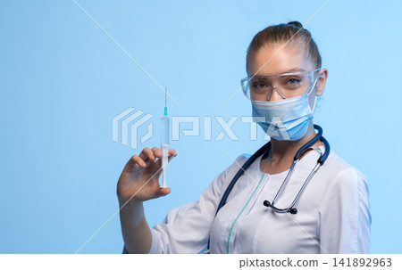 Healthcare worker holding a syringe, preparing for vaccination, treatment, or medical injection on a blue background Healthcare worker holding a syringe, preparing for vaccination, treatment, or medical injection on a blue background 141892963