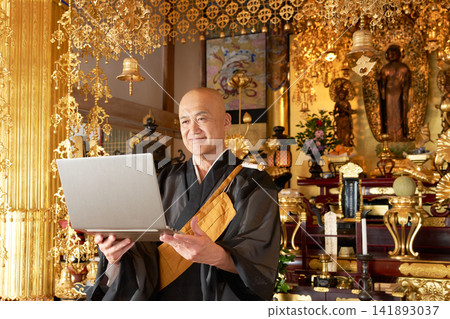 一位僧人在大殿裡看著筆記型電腦螢幕。 一位僧人在大殿裡看著筆記型電腦螢幕。 141893037