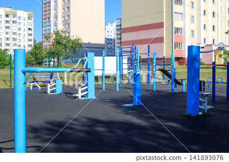 Municipal sports ground with exercise equipment next to residential buildings. Various sports equipment on a playground Municipal sports ground with exercise equipment next to residential buildings. Various sports equipment on a playground 141893076