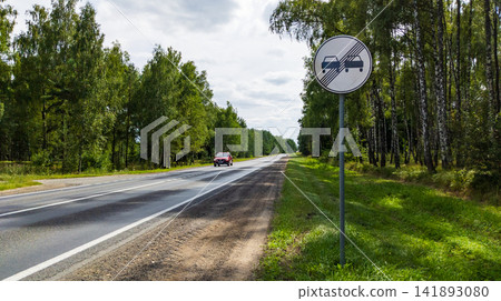 Road Sign End of Overtaking Restriction Symbol on Highway Near Forest with Car Road Sign End of Overtaking Restriction Symbol on Highway Near Forest with Car 141893080