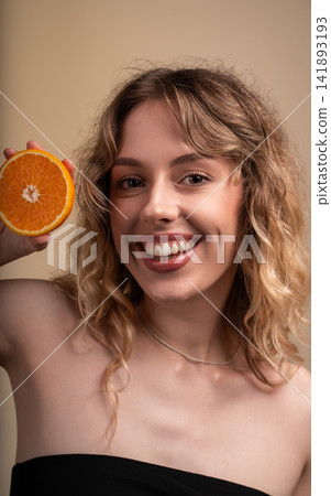Happy woman holding orange showing healthy lifestyle, vitamin C, and fresh skincare concept with radiant smile Happy woman holding orange showing healthy lifestyle, vitamin C, and fresh skincare concept with radiant smile 141893193