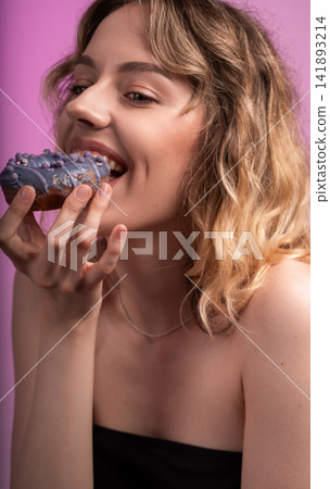 Young woman enjoying sweet purple glazed donut, biting into indulgent pastry snack, smiling Young woman enjoying sweet purple glazed donut, biting into indulgent pastry snack, smiling 141893214