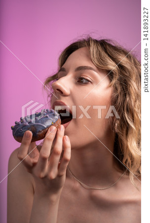 Young woman enjoying sweet purple glazed donut with sprinkles, indulging in a sugary craving and temptation Young woman enjoying sweet purple glazed donut with sprinkles, indulging in a sugary craving and temptation 141893227