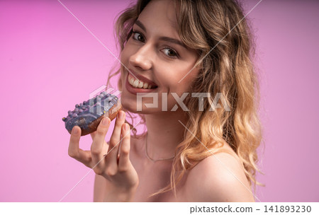 Young woman smiling and holding a purple glazed donut, celebrating happiness with a sweet sugar snack Young woman smiling and holding a purple glazed donut, celebrating happiness with a sweet sugar snack 141893230