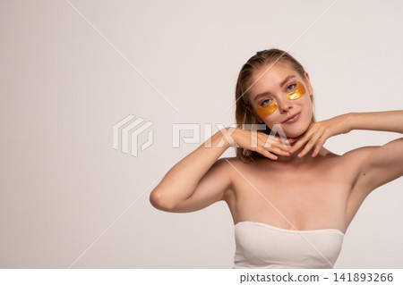 Young woman applying golden eye patches for skincare and beauty routine, getting facial treatment for healthy skin Young woman applying golden eye patches for skincare and beauty routine, getting facial treatment for healthy skin 141893266