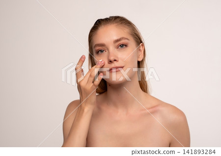 Young woman applying face cream, moisturizing healthy skin for a daily beauty and wellness routine Young woman applying face cream, moisturizing healthy skin for a daily beauty and wellness routine 141893284
