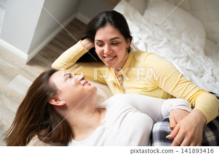 Two women relaxing together on a cozy bed in a warmly lit home interior. Friendship sisterhood family bonding and emotional support between women Two women relaxing together on a cozy bed in a warmly lit home interior. Friendship sisterhood family bonding and emotional support between women 141893416