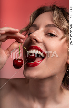 Woman with bright red lips holding and biting into fresh cherries, enjoying ripe healthy fruit and sensual beauty 141893446