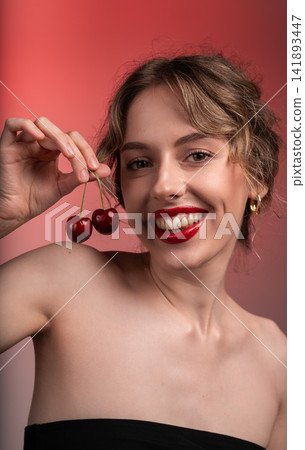 Woman holding cherries, smiling with red lips, expressing joy, beauty, and healthy eating against a vibrant background Woman holding cherries, smiling with red lips, expressing joy, beauty, and healthy eating against a vibrant background 141893447