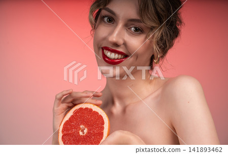 Young woman smiling, holding grapefruit, promoting healthy skin and natural beauty with red lips Young woman smiling, holding grapefruit, promoting healthy skin and natural beauty with red lips 141893462