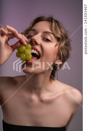 Young woman enjoying fresh green grapes, promoting healthy eating and natural beauty in a studio setting Young woman enjoying fresh green grapes, promoting healthy eating and natural beauty in a studio setting 141893467