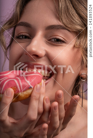 Young woman enjoying a sweet pink donut, biting into sugary pastry with a joyful smile and happy expression Young woman enjoying a sweet pink donut, biting into sugary pastry with a joyful smile and happy expression 141893524