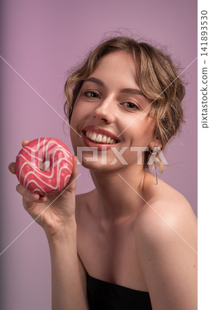 Young woman smiling and holding a delicious pink glazed donut, symbolizing joy, indulgence, and sweet treat pleasure Young woman smiling and holding a delicious pink glazed donut, symbolizing joy, indulgence, and sweet treat pleasure 141893530